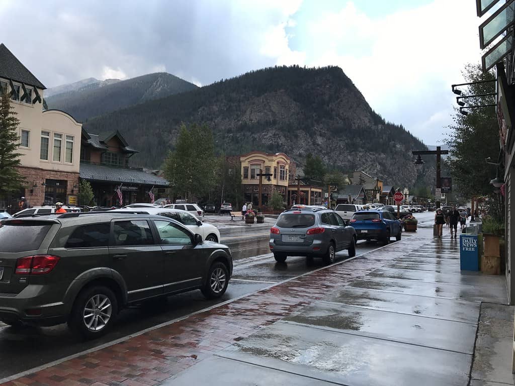 Main Street Frisco, CO, on a rainy day with pedestrians and commercial buildings lining the street and a mountain and overcast in the background