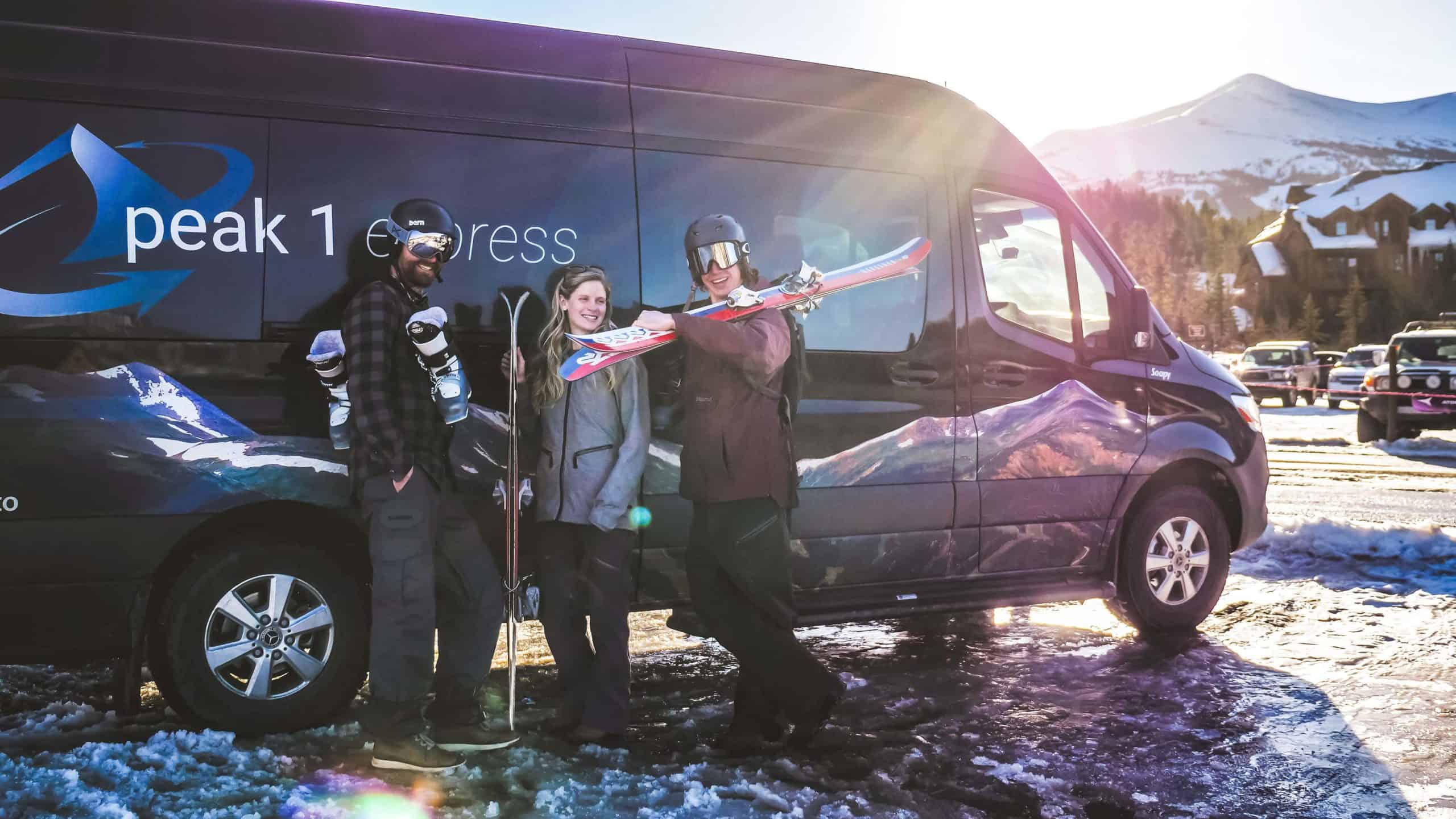 Friends standing beside a peak 1 express van in a ski resort parking lot