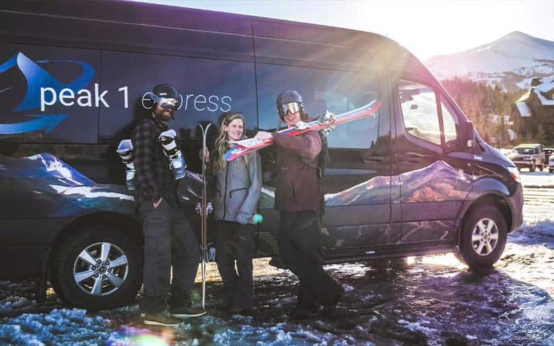 Three people standing in front of a shuttle with ski gear