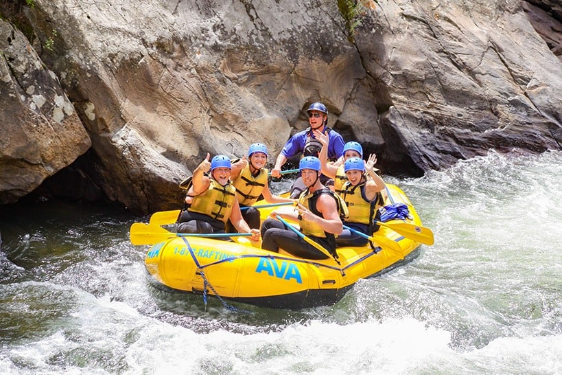 Rafters in a yellow raft marked AVA smiling and waving at a camera