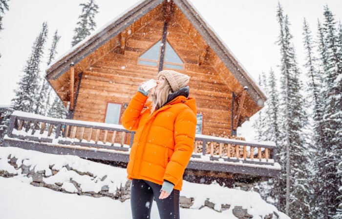 woman drinking milk outside of a cabin in the winter